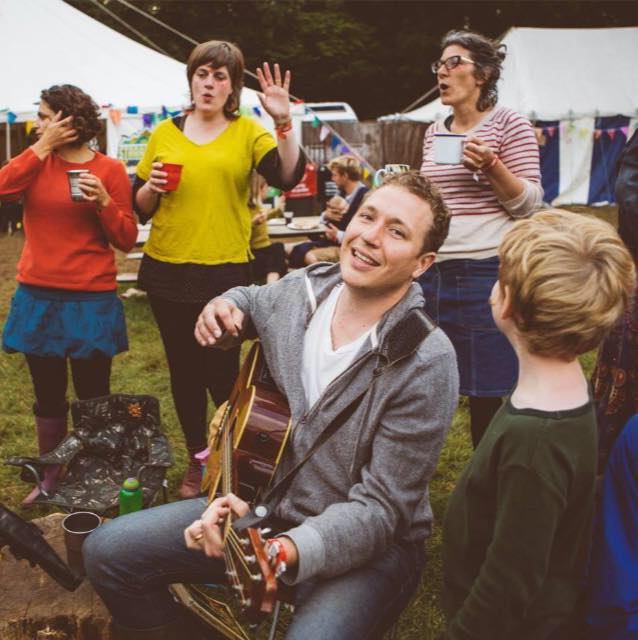 Andy Hawkings playing guitar as a group of people sing along at a festival